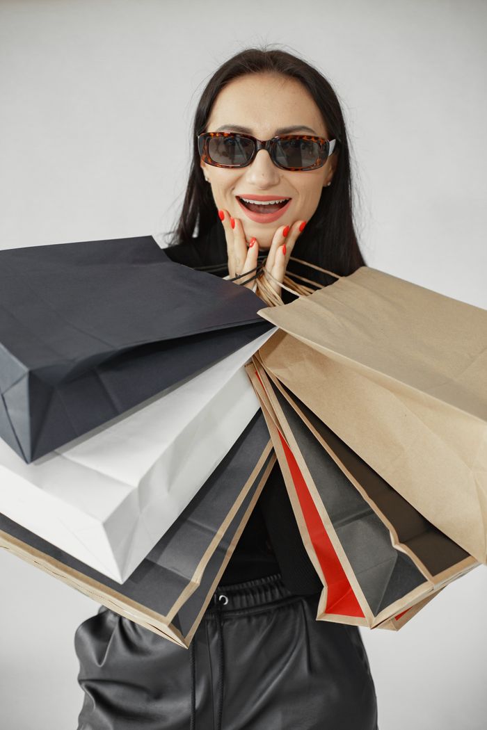 gallery-6 Fashionable woman with sunglasses excitedly holding multiple shopping bags indoors.