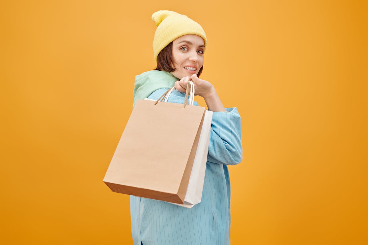 services-img Cheerful woman in beanie holding shopping bags against vibrant orange backdrop.