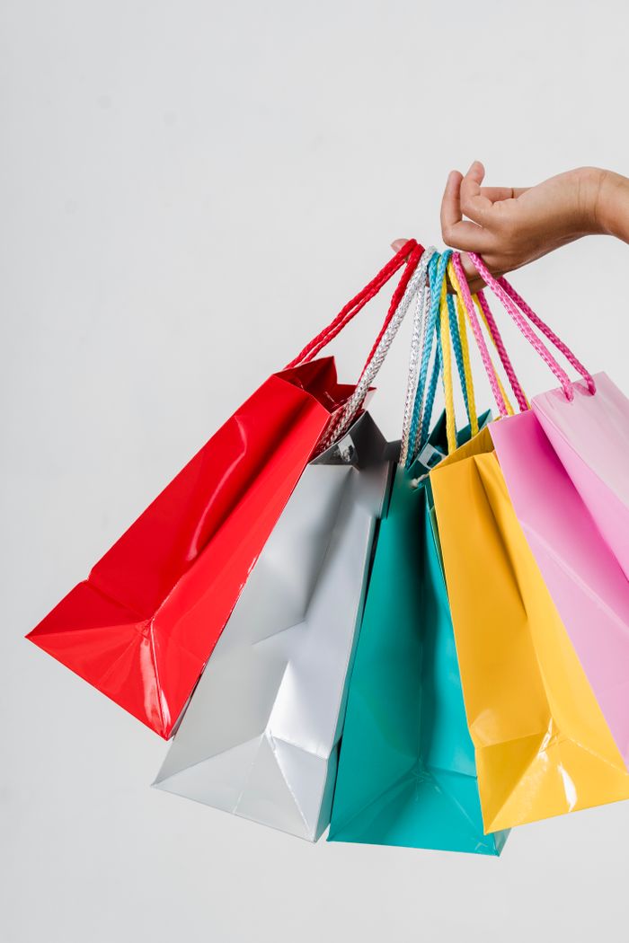 hero-img-02 Close-up of a hand holding multiple colorful shopping bags on a white backdrop, perfect for retail or consumerism concepts.