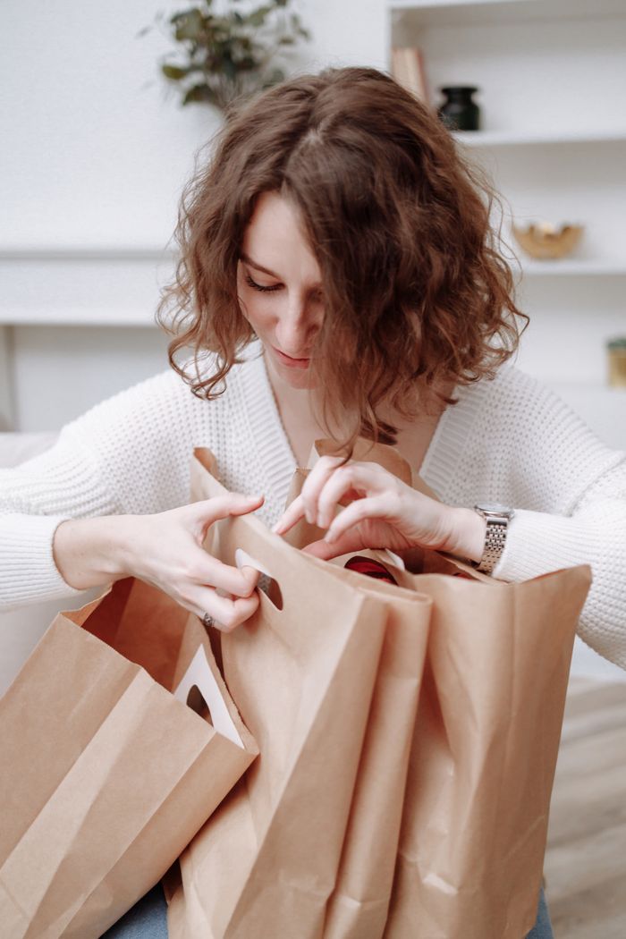 services-01 A woman in a white sweater looks into shopping bags indoors, creating a cozy, minimalist vibe.