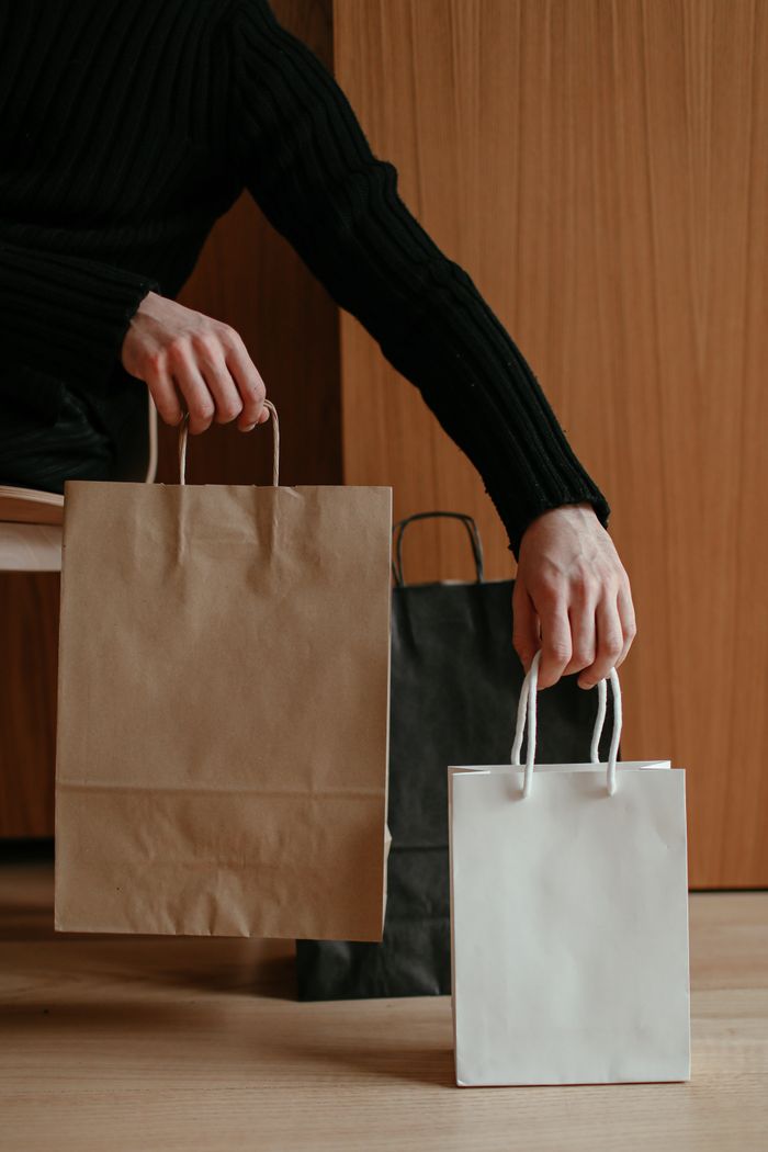 services-02 Person holding brown and white paper shopping bags indoors, focusing on minimalistic lifestyle.